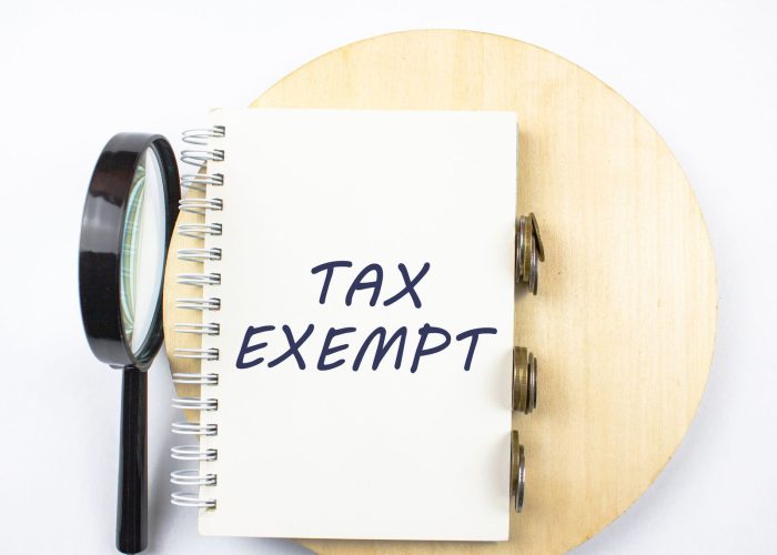 Words TAX EXEMPT written in a notepad next to coins and a magnifying glass.The concept of exempting a business, company, organization from paying taxes